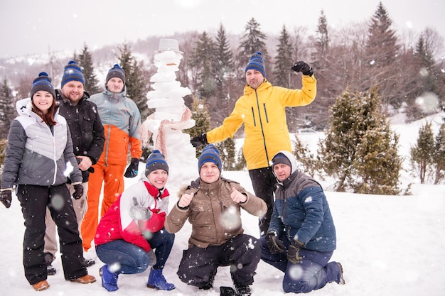 ritratto di gruppo di giovani uomini d'affari felici dopo una competizione in posa con un pupazzo di neve finito mentre si godono una giornata invernale innevata con fiocchi di neve intorno a loro durante un team building nella foresta di montagna