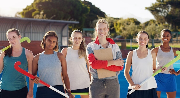 Ritratto di hockey e un allenatore sportivo con la sua squadra in piedi insieme all'aperto per l'allenamento o una partita Diversità del lavoro di squadra e coaching con un'allenatrice all'aperto con un gruppo di ragazze per lo sport