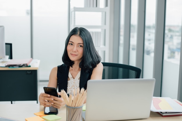 Ritratto di imprenditrice asiatica di successo utilizzando il telefono e lavorando presso un ufficio moderno