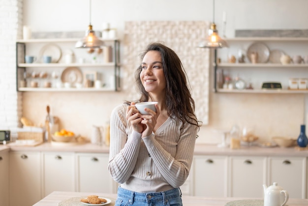 Ritratto di inizio giornata di donna allegra che si gode il caffè del mattino tenendo la tazza in mano in piedi