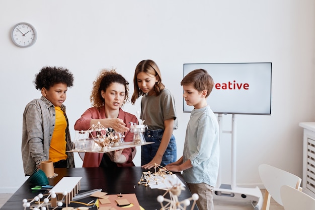 Ritratto di insegnante femminile che aiuta i bambini a realizzare modelli in legno durante le lezioni di arte e artigianato a scuola