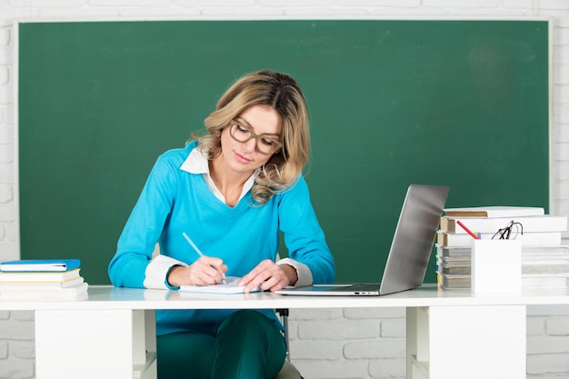 Ritratto di insegnante femminile di insegnante o tutor femminile che lavora a tavola al college o al liceo giovane