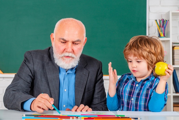 Ritratto di insegnante senior e ragazzino seduto alla scrivania in classe allievo e insegnante in classe