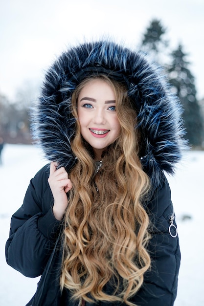 Ritratto di inverno della giovane donna. Dof poco profondo. Bel volto sorridente di modella con labbra rosse e cappuccio di pelliccia