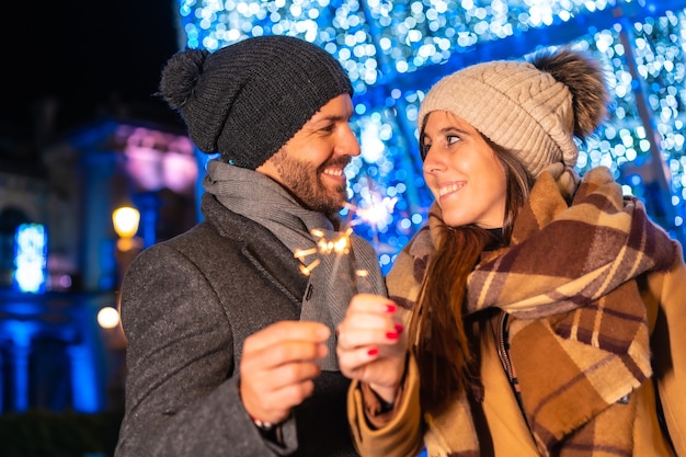 Ritratto di inverno di una coppia caucasica che gode delle luci di Natale con le torce in mano