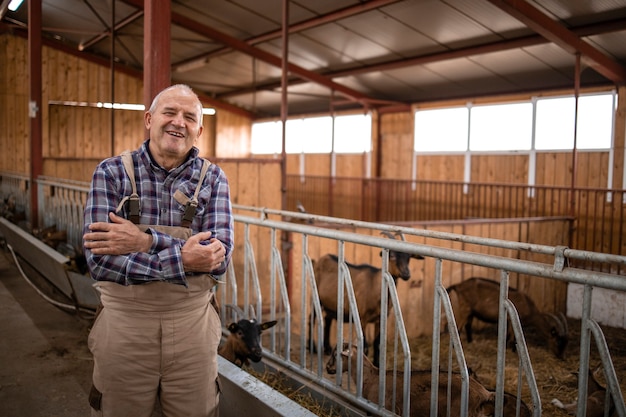 Ritratto di lavoratore agricolo senior con le braccia incrociate in piedi in fattoria