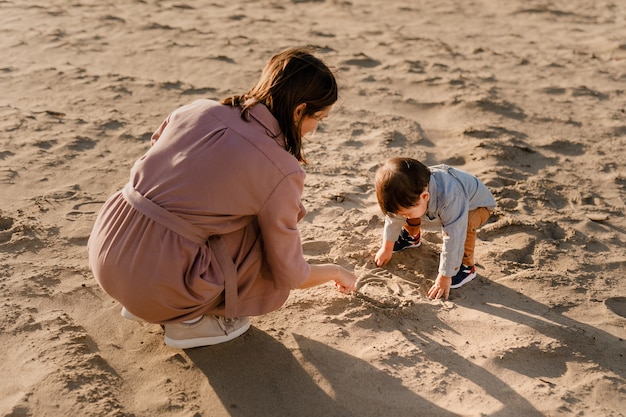 Ritratto di madre amorevole e suo figlio di un anno che cammina e gioca con la sabbia.