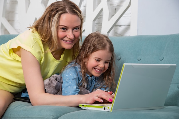 ritratto di madre con figlia sdraiata sul divano con un laptop e guarda il monitor con un sorriso.