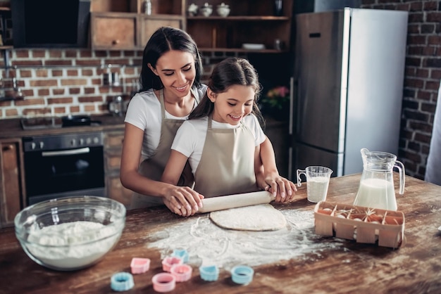 Ritratto di madre e figlia che stendono un impasto con il mattarello in cucina