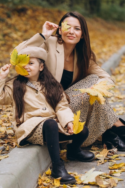 Ritratto di madre e figlia felici che trascorrono del tempo insieme nel parco autunnale con foglie gialle che cadono