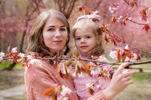 Ritratto di madre e figlia nel parco con sakura rosa in fiore