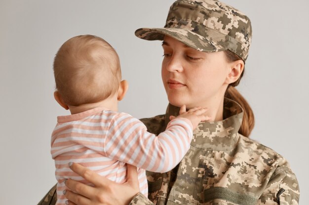 Ritratto di madre militare emotiva, vestita in mimetica, che tiene in braccio la sua giovane figlia, salutando dopo il ritorno a casa da un tour di servizio all'estero.