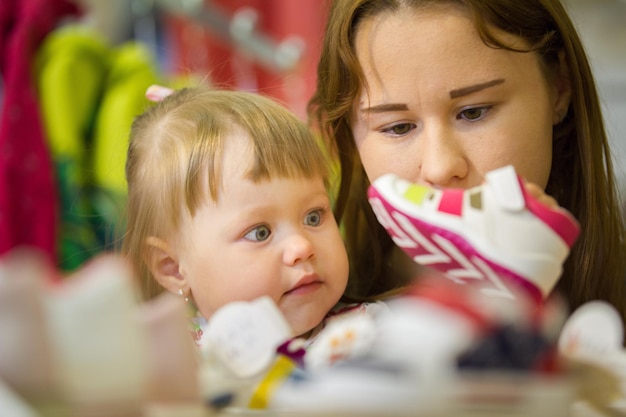 Ritratto di mamma con figlia che sceglie le scarpe al negozio per bambini