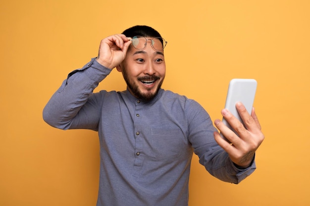 Ritratto di maschio asiatico stupito che toglie gli occhiali e guarda lo smartphone
