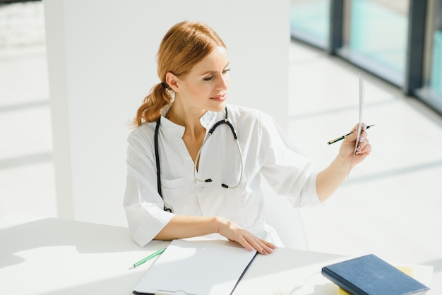 Ritratto di medico femminile attraente che tiene appunti mentre levandosi in piedi in clinica