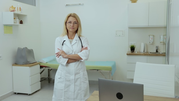 Ritratto di medico femminile sicuro che sta nell'ufficio medico dell'ospedale che guarda l'obbiettivo con lo stetoscopio. Medico in uniforme in clinica.