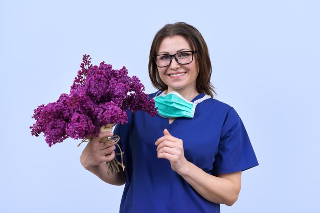 Ritratto di medico femminile sorridente maturo in occhiali con maschera medica protettiva che tiene bouquet di fiori. Giornata del medico, Giornata mondiale della salute, Giornata nazionale degli infermieri