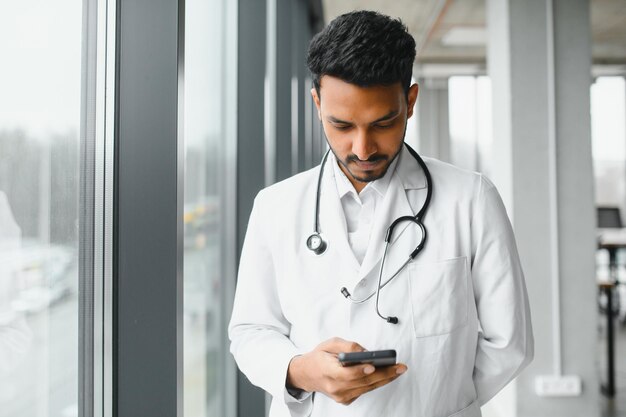 Ritratto di medico indiano maschio che indossa camice bianco con porta aperta sul corridoio della clinica come sfondo