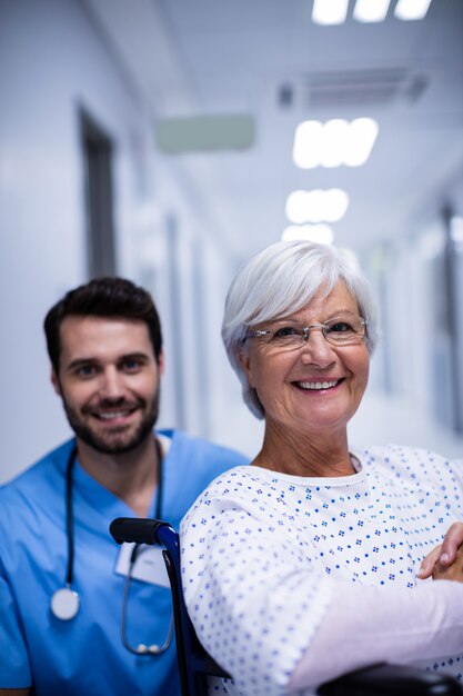 Ritratto di medico maschio e paziente senior femminile che sorridono nel corridoio