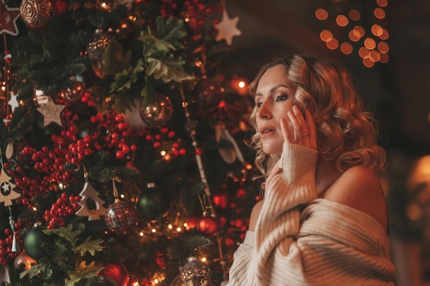 Ritratto di millenaria candida autentica signora in maglione beige lavorato a maglia in posa sognante da sola all'albero di Natale