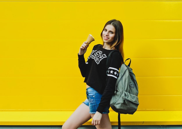 Ritratto di moda all'aperto di giovane ragazza hipster con gelato su sfondo muro giallo