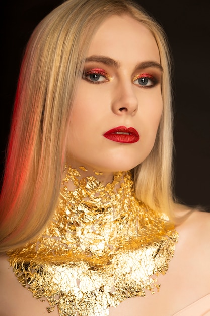 Ritratto di moda del primo piano di una bella donna bionda con labbra rosse e lamina d'oro sul collo