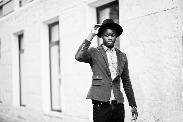 Ritratto di moda dell'uomo afroamericano nero su giacca di velluto verde e cappello nero che cammina per le strade della casa di sfondo della città con molte finestre BW foto