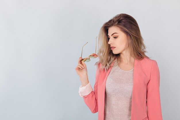 Ritratto di moda di un'attrattiva donna bionda elegante con una giacca rosa casuale pastello che posa in studio