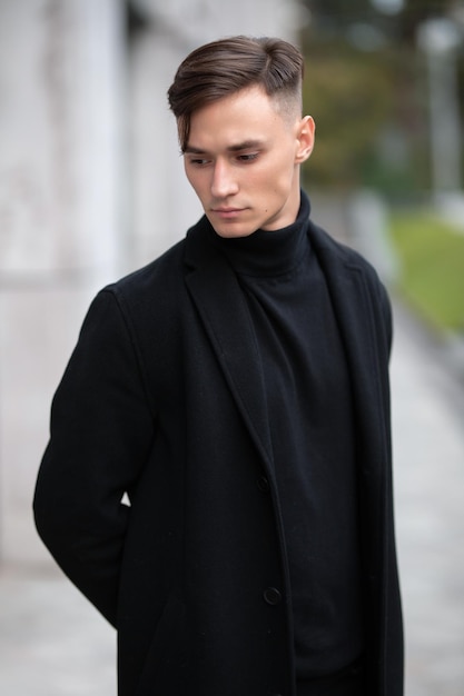Ritratto di moda di un giovane ragazzo in abiti neri di aspetto del modello per strada