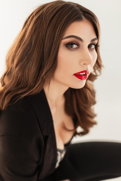 Ritratto di moda di un modello di bella giovane donna con trucco e labbra rosse in abiti eleganti neri alla moda su sfondo bianco. Volto femminile di bellezza naturale