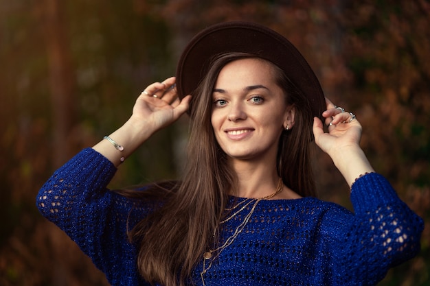 Ritratto di moda elegante boho chic donna con cappello e maglia maglione blu nella foresta di autunno