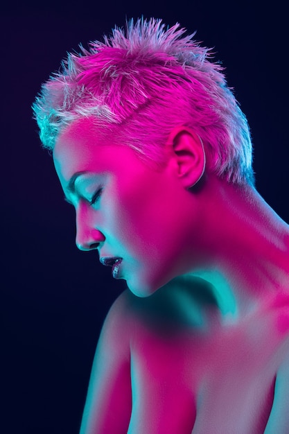 Ritratto di modella femminile in luce al neon su sfondo scuro studio.