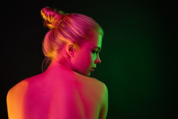 Ritratto di modella femminile in luce al neon su sfondo scuro studio.