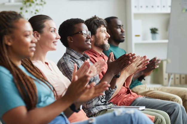 Ritratto di multietnico gruppo di persone che applaudono seduti in fila in udienza o sala conferenze