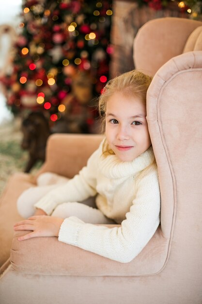 Ritratto di Natale della ragazza felice bambino biondo in maglione bianco ubicazione sul pavimento