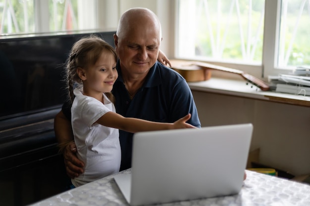 Ritratto di nonno e nipote che fanno i compiti con il computer portatile.