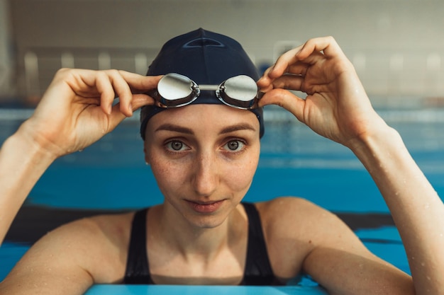 Ritratto di nuotatrice professionista in cuffia che regola gli occhialini da nuoto e guarda la fotocamera