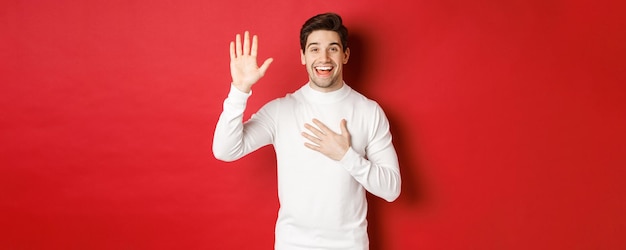 Ritratto di onesto uomo sorridente in maglione bianco che fa una promessa giurando di dire la verità in piedi aga