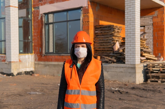 Ritratto di operaia edile femminile in maschera medica e tuta sullo sfondo della casa in costruzione