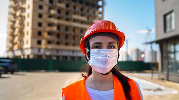 Ritratto di operaia edile femminile in maschera medica e tuta sullo sfondo della casa in costruzione