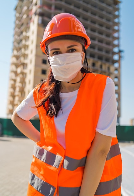 Ritratto di operaia edile femminile in maschera medica e tuta sullo sfondo della casa in costruzione