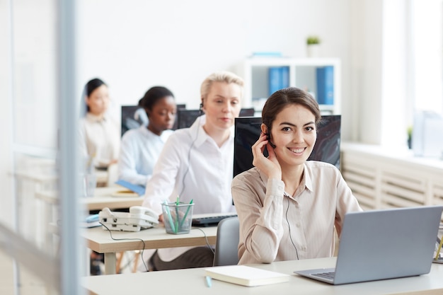 Ritratto di operatori di helpdesk femminile seduti in fila, concentrarsi sulla donna sorridente che guarda mentre parla al cliente tramite auricolare