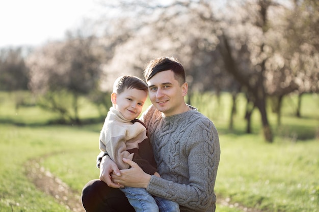 Ritratto di padre e figlio in maglioni lavorati a maglia sullo sfondo di un albero in fiore in primavera