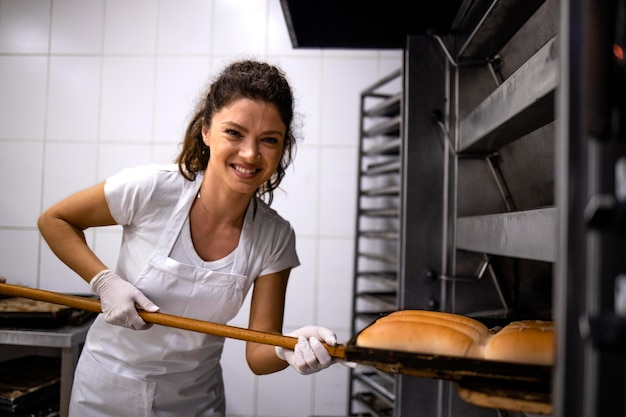Ritratto di panettiere femminile che tiene vassoio di legno e mette il pane nel forno nel forno