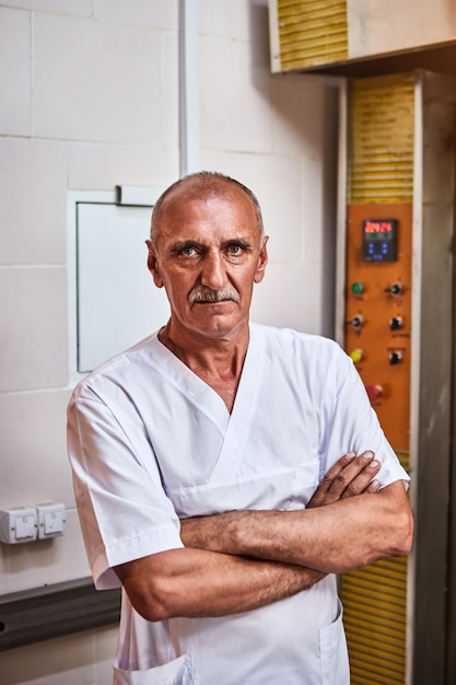 Ritratto di panettiere professionista in uniforme si trova sullo sfondo di un forno industriale in una panetteria per fare il pane