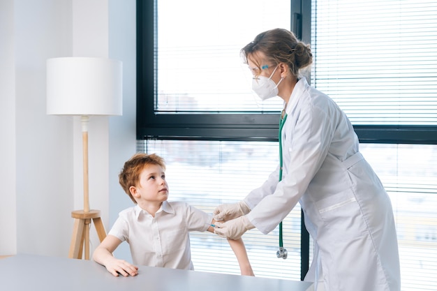 Ritratto di pediatra femminile che indossa l'uniforme bianca che applica il gesso sulla spalla del bambino dopo l'iniezione di vaccinazione tramite finestra