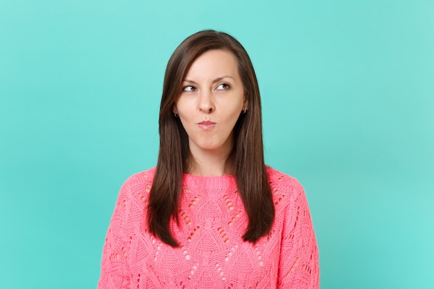 Ritratto di pensieroso interessato giovane donna in maglia maglione rosa cercando da parte isolato su sfondo blu muro turchese in studio. Persone sincere emozioni, concetto di stile di vita. Mock up copia spazio.