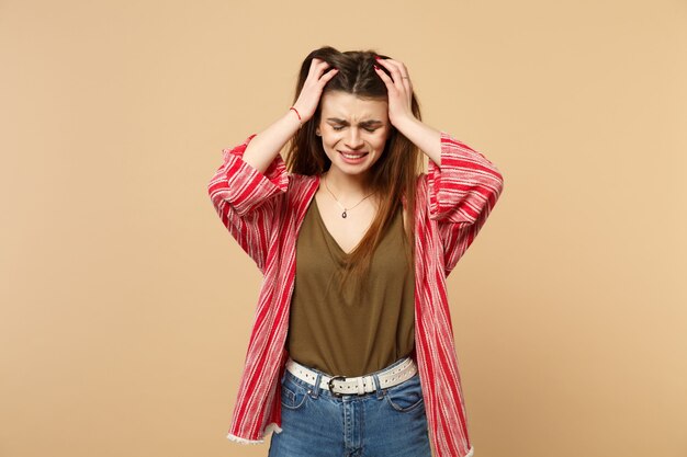 Ritratto di pianto dispiaciuto giovane donna in abiti casual che mette le mani sulla testa isolata sul fondo della parete beige pastello in studio. Persone sincere emozioni, concetto di stile di vita. Mock up copia spazio.