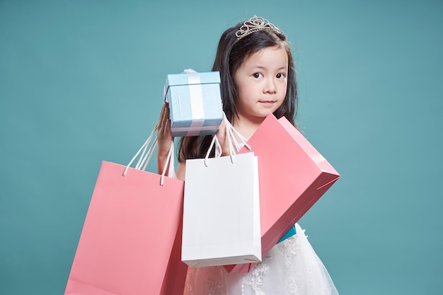 Ritratto di piccola bella ragazza asiatica che tiene scatola attuale e borsa della spesa su sfondo blu vintage