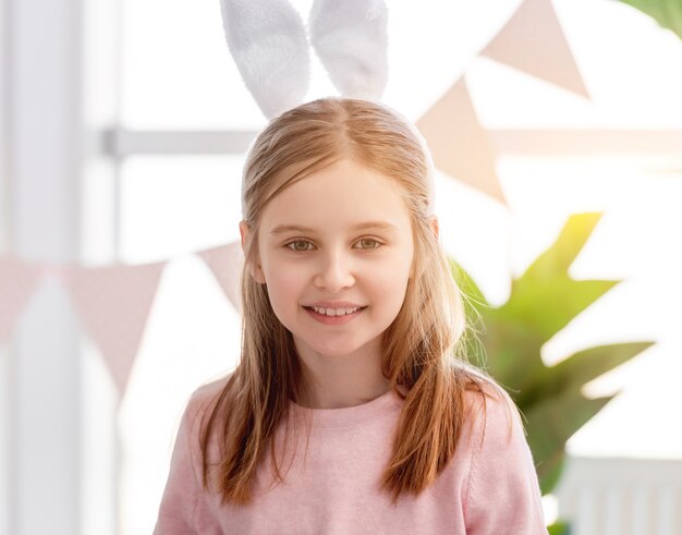 Ritratto di piccola bella ragazza che indossa orecchie da coniglio e stare nella stanza piena di luce solare